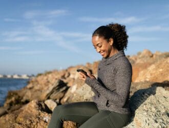 "Woman using mental health app on phone outdoors near sea