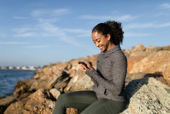 "Woman using mental health app on phone outdoors near sea